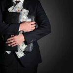 Businessman hugging briefcase stuffed with cash