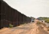 Border fence beside a dusty desert road with trucks