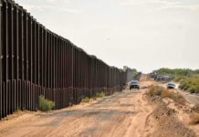 Border fence beside a dusty desert road with trucks