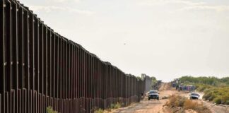 Border fence beside a dusty desert road with trucks