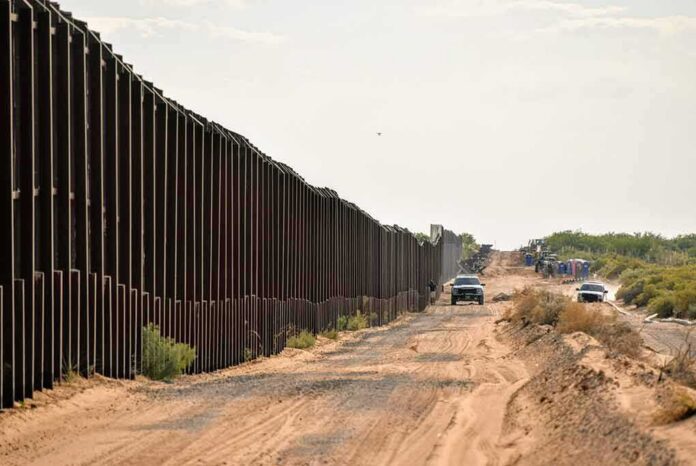 shutterstock_1545827498 Border fence beside a dusty desert road with trucks