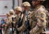 Soldiers in camouflage gear stand in formation holding rifles