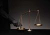 Golden balance scale with gloved hand pressing one pan