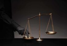 Golden balance scale with gloved hand pressing one pan
