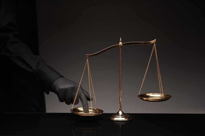Golden balance scale with gloved hand pressing one pan