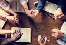 Judge Criminalizes Christian Flyers – Convicts Street Evangelist Group holding hands around open books on a wooden table