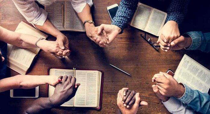 shutterstock_1081710347 Group holding hands around open books on a wooden table