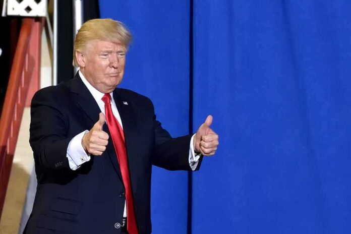shutterstock_1087344797 Donald Trump giving two thumbs up in front of a blue curtain