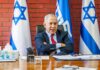 man in suit seated at a desk with Israeli flags behind him