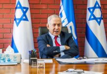man in suit seated at a desk with Israeli flags behind him