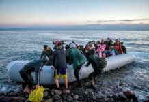 Smugglers Adapt — Overloaded Dinghies Group of people arriving on a crowded inflatable boat at a rocky shore