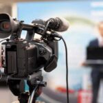 Collins-Mulvaney Twist Stuns WH Dinner video camera filming a speaker at a podium