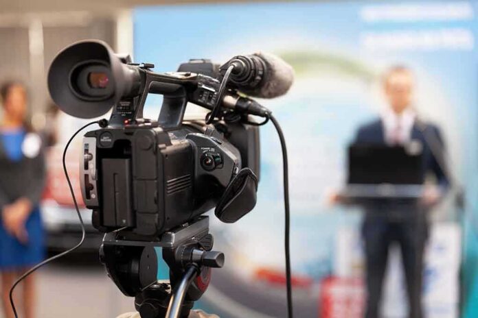 shutterstock_1674487702 video camera filming a speaker at a podium