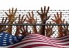 Hands reaching through a chain-link fence topped with barbed wire
