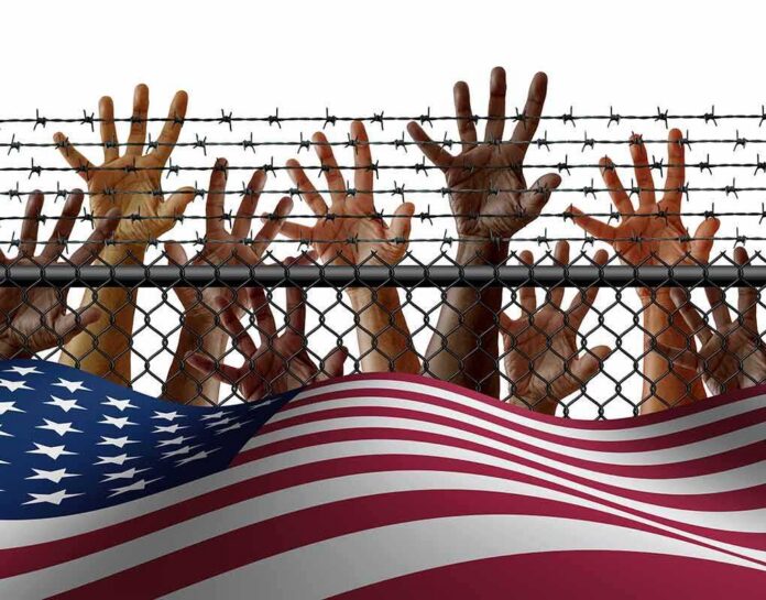 Hands reaching through a chain-link fence topped with barbed wire