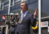 Gavin Newsom speaks at a press conference with microphones outside a building
