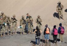 Soldiers stand behind barbed wire facing civilians
