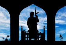 Blurred Labels, Deadly Blindspots: The Real Jihad Engine Silhouette of armed person standing before arches with mosque and palm trees at sunset sky