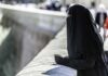 Person in black veil leaning on a stone railing