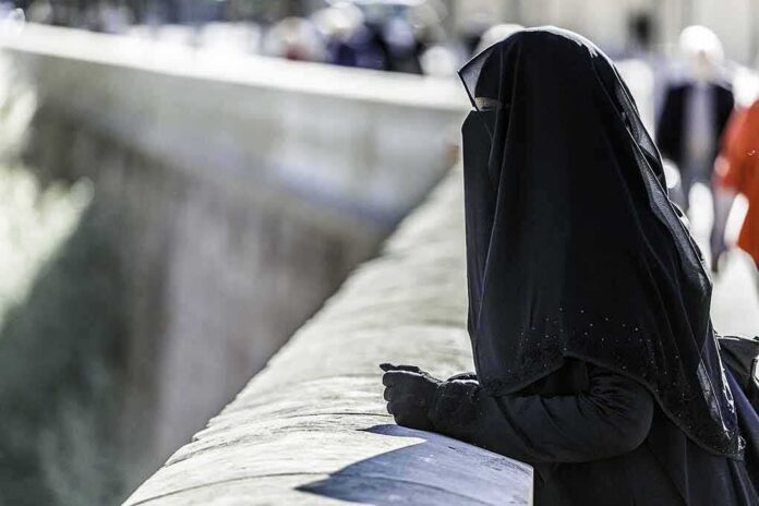 shutterstock_595364105 Person in black veil leaning on a stone railing