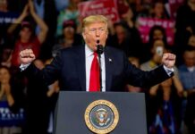 Senator’s Defiant Texts Jolt MAGA Donald Trump speaking at a rally podium with arms raised