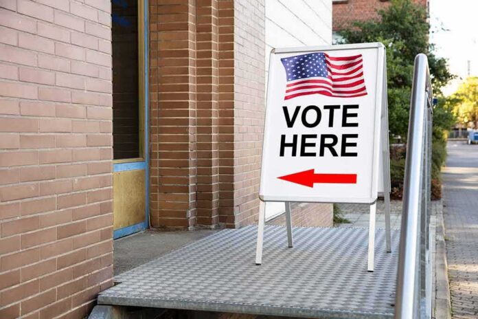 shutterstock_1239383353-1 Sidewalk sign with American flag directing to a polling place