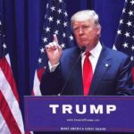 FISA Failures Resurface In Trump Appeal man in suit speaking at podium with multiple American flags