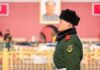 uniformed guard in green coat and fur hat standing in profile outdoors