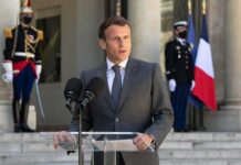 man in suit speaking at podium with microphones