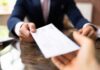 Racial Pay Boosts Trigger Legal Minefield Businessperson handing over a check across a desk