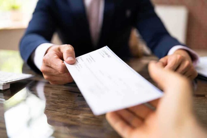 shutterstock_2153663501 Businessperson handing over a check across a desk