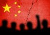 Factory Ghost Towns – China Pay Meltdown Hits Supply Chains Chinese flag with crack and crowd silhouettes
