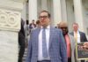 Kabuki Congress Exposed – Fraudster Blows Whistle On Capitol Circus man in a blue plaid suit walking down marble steps