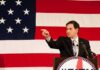 UN War-Crime Shock – Rubio Fires Back Speaker in suit pointing during speech before large American flag