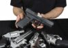 Person holding a black semi-automatic pistol over several revolvers