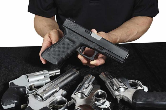 Person holding a black semi-automatic pistol over several revolvers