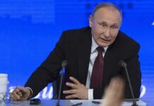 Vladimir Putin speaking at a press conference table with microphones